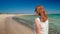 Back View of Woman Walking along Sea Shore on Sand Beach in Summer in Greece