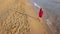 Back view of a woman walking barefoot along wet sand beach. Running wave is washing away footprints on the sand