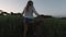 Back view of woman walking through a field touching green high grass