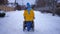 Back view woman walking on winter road pushing wheelchair with man on snow. Confident caring Caucasian wife taking care