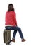 Back view of womanin cardigan sitting on a suitcase.