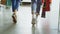 Back view of women`s legs going slowly through spacious shop. Girls are wearing jeans and trainers and carrying