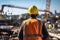 Back view of worker in orange safety vest and yellow helmet overseeing construction site