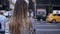 Back view of young beautiful woman crossing the road in New York, America. Female looking on the riding cars and taxi.