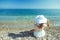 The back view of young beautiful woman in white dress sitting on the beach and looking at the sea horizon