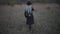 Back view of young blonde girl dressed in black, wearing hat, coat and backpack. Walking in dry field.