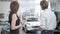 Back view of young Caucasian man and woman looking at new luxurious cars in dealership and talking. Professional dealer
