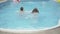 Back view of young Caucasian man and woman swimming in outdoor water pool at luxurious resort. Wealthy confident couple