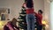 Back view young Caucasian woman decorating Christmas tree with sister and mother. Happy family preparing house for New