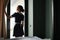 Back view of young chambermaid in uniform opening curtains in hotel room