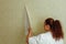 Back view of young fat woman wearing white T-shirt, beige trousers, standing at wall, removing old yellow wallpaper.