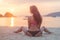 Back view of young female with long brown hair sitting on beach legs spread far apart in black bikini panties admiring