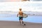 Back view of young fit surfer man with surfboard runs into ocean or sea with big waves for surfing. Concept of extreme