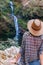 Back view of young girl in straw hat and looking at waterfall. Caucasian young lady looks at falling water, photo on