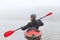 Back view of young handsome man kayaking in river, spends foggy morning in canoe, extreme sport, man in black jacket and gray cap