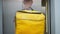 Back view young male courier with yellow thermal bag entering elevator in house or business center. Caucasian man