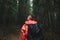 Back view of a young male hiker with a travel backpack wearing a red raincoat looking at the mountain forest. Rainy weather,