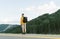 Back view of young male hiker in yellow sweatshirt observing the green fir forests in the mountains. Tourist guy with backpack