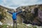 Back view Young man hiker with backpack standing on top of the mountain with raised hands enjoying rocks landscape. Travel