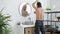 Back view of young man in pajamas pants shaving armpits with razor in bathroom