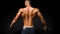 Back view of young man shirtless portrait training with dumb-bell against black background.