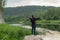 Back view of young man tourist with arms opened wide on bank mountain river. Tourism, hiking, active leisure. Discovering world