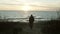 Back view of young man walking on the shore of the sea on sunset. Lonely male spending time alone in beach in cold day.