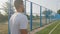 Back view Young Middle eastern Arabic athlete in summer sportswear white t-shirt walking moving along stadium fence