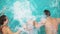 Back view of young mother and father together with their child jumping in the swimming pool holding hands. Mother and