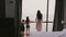 Back view young mother and two happy children stand together at large hotel room window staring at sea view slow motion.