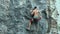 Back view young muscular man rock climber climbing on tough sport route outdoors on a vertical cliff