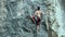 Back view young muscular man rock climber climbing on tough sport route outdoors on a vertical cliff