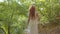 Back view of a young nice woman dressed in light white clothes walking in the autumn forest with a straw basket