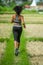 Back view of young runner woman with attractive and fit body in running outdoors workout at beautiful off road track green landsca