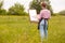Back view of young slim woman artist drawing picture on canvas in nature, girl with brush in hand and palette of paints working on