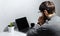 Back view of young thoughtful businessman with pencil on ear, looking in laptop, using wireless earphones, wearing smartwatch.