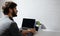 Back view of young thoughtful businessman working home, making notes in notebook, using wireless earphones, laptop, coffee mug.