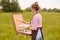 Back view of young woman artist standing in front of sketchbook with brush and palette of colours, paints picture in nature in