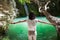 Back view of young woman with hands up enjoy waterfall on beautiful lake