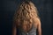 Back view young woman with long blond curly hair at back on studio background.