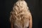 Back view young woman with long blond curly hair at back on studio background.