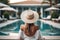 Back view of young woman with long blond hair wearing white straw hat on poolside in her vacation at a beautiful resort. Summer