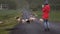 Back view of young woman standing on the road and taking photos of sheep grazing on the field o smartphone.