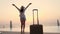 Back view of young woman in summer clothes and sun hat, with travel luggage, standing at the pool, enjoying the sunrise