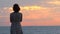 Back view of young woman in summer dress looking at the sea, enjoying the sunrise, against the background of sunrise and
