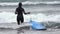 Back view of young woman surfer pulling blue surfboard by leg rope walking knee deep in breaking waves of Pacific Ocean