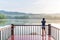 Back view of young woman taking photograph on the wooden balcony and looking at lake on morning