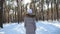 Back view of young woman walking in sunny winter forest. Unrecognisable girl enjoying stroll through snowy wood