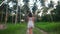 Back view of young woman in white dress walking in jungle among palm trees on tropical island