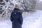 Back of woman in hat with pompom walking on path in snowy forests. Alone person in snow weather